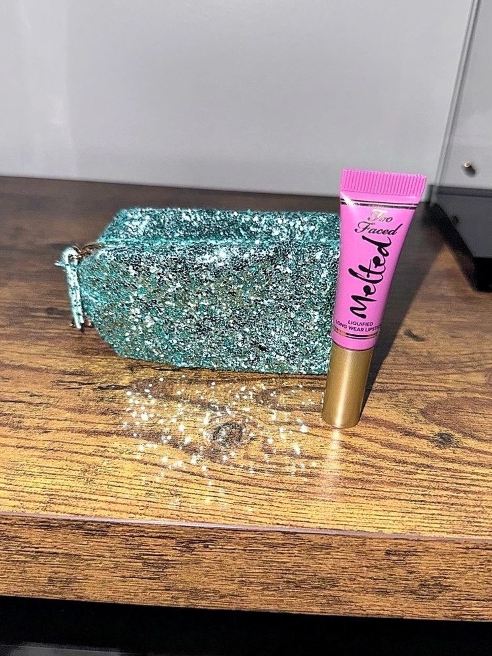 Too Faced Melted Liquified Long Wear Lipstick tube alongside a teal, glittery